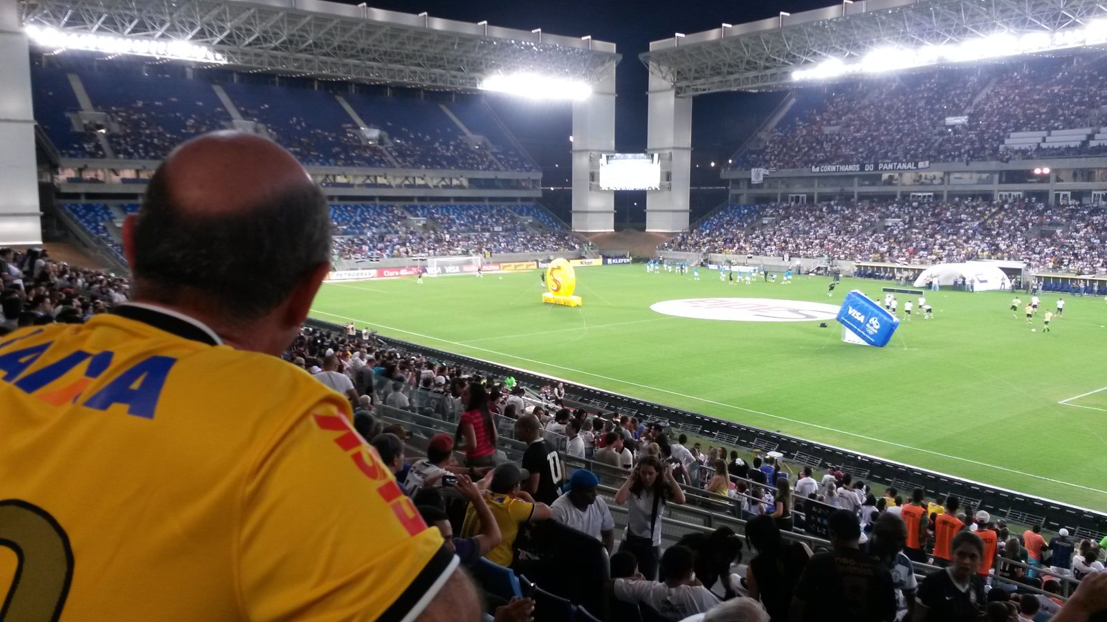 Vista interna da Arena Pantanal, em Cuiabá (MT), com torcida e gramado durante partida.