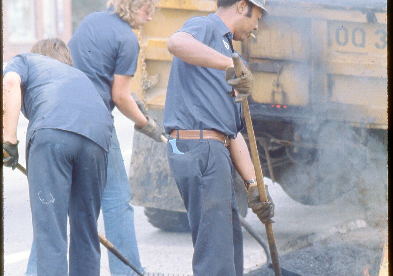 Trabalhadores aplicando asfalto em obra de pavimentação