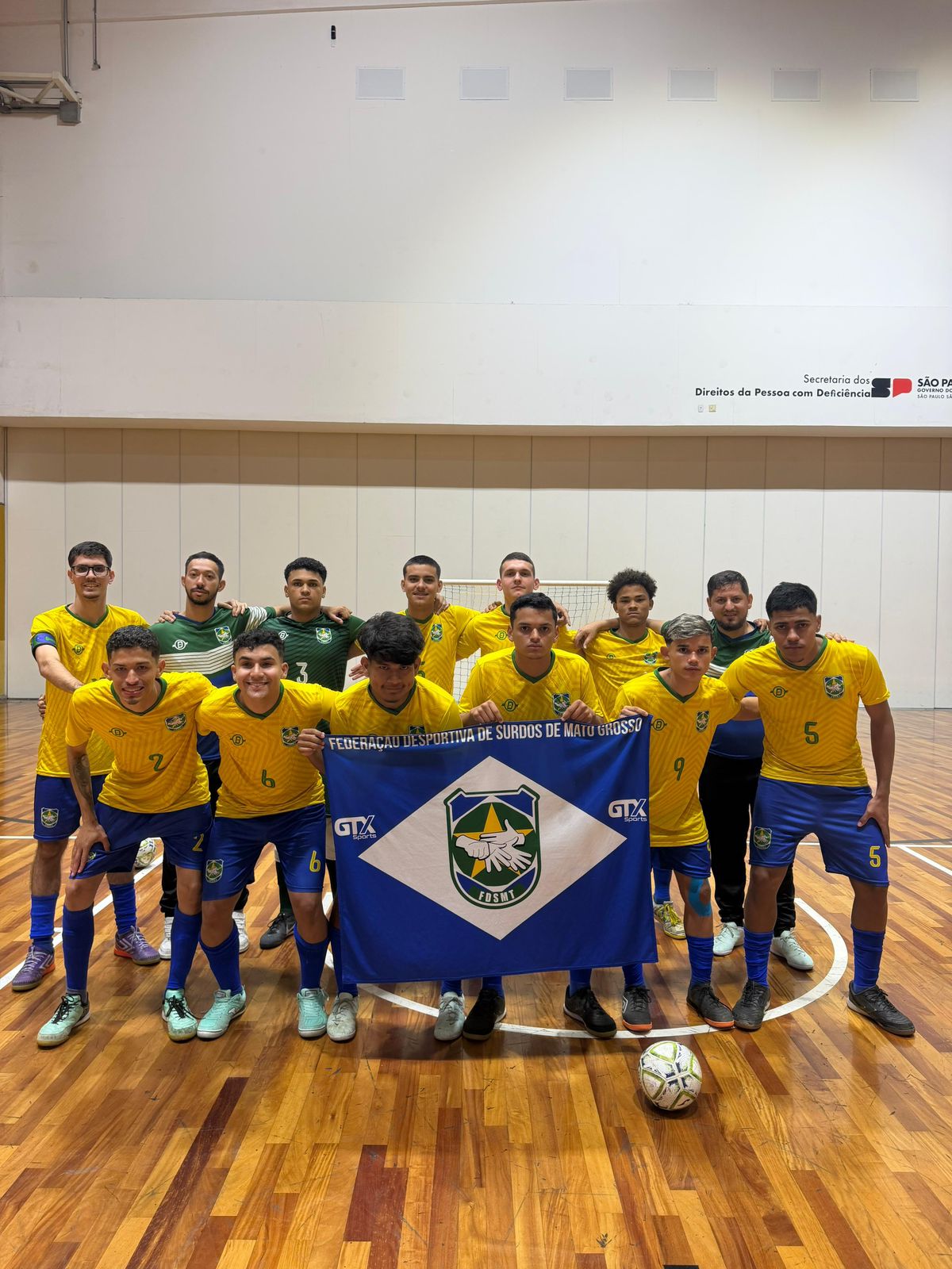 Atletas mato-grossenses de futsal de surdos com a bandeira da FDSMT na quadra
