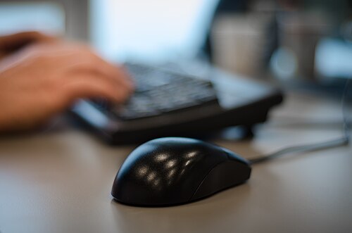 Mãos digitando em teclado de computador em mesa de escritório