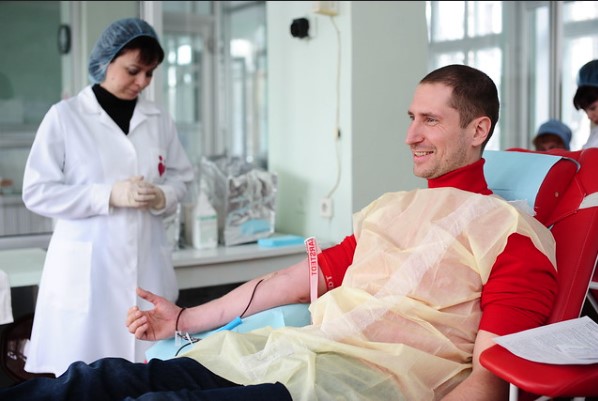 Pessoa doando sangue em ambiente hospitalar acompanhada por profissional de saúde