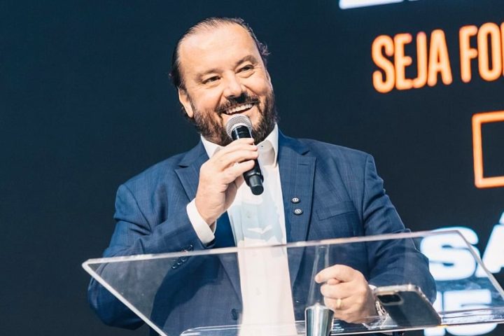 Reinaldo Morais discursa ao microfone, atrás de um púlpito de acrílico, durante evento