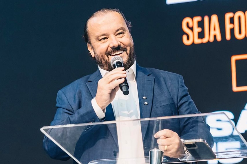Reinaldo Morais discursa ao microfone, atrás de um púlpito de acrílico, durante evento