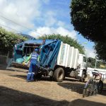 Caminhão de coleta de lixo com trabalhador uniformizado recolhendo sacos na rua