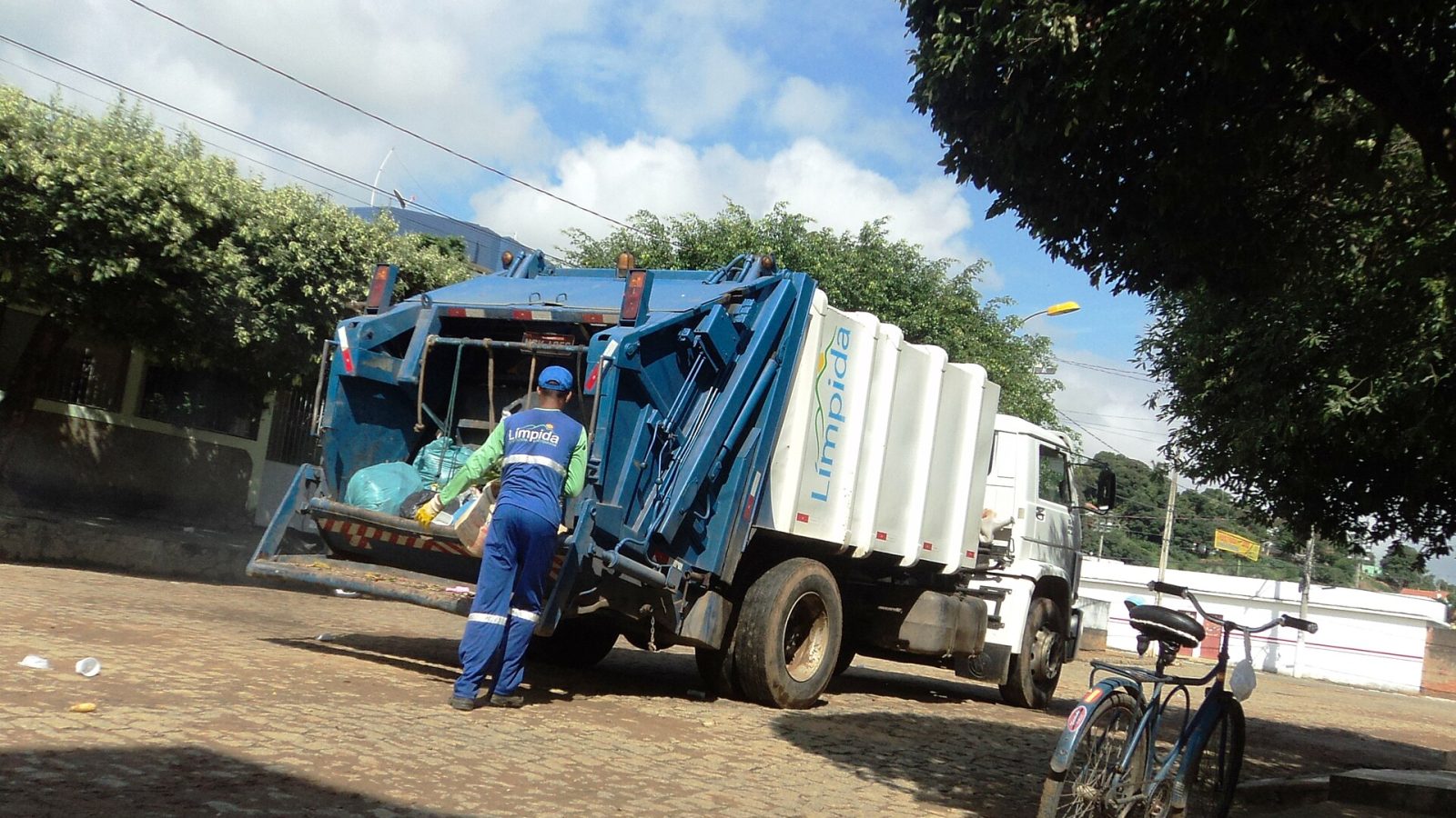 Caminhão de coleta de lixo com trabalhador uniformizado recolhendo sacos na rua