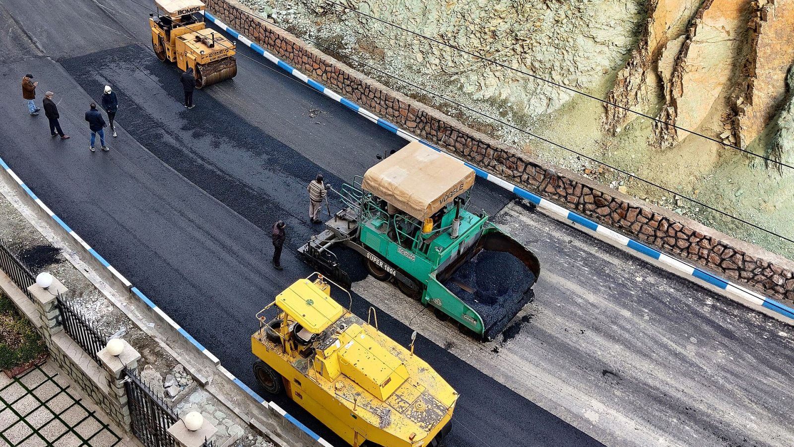 Vibroacabadora e rolos compactadores aplicando asfalto em trecho de rodovia, vistos do alto