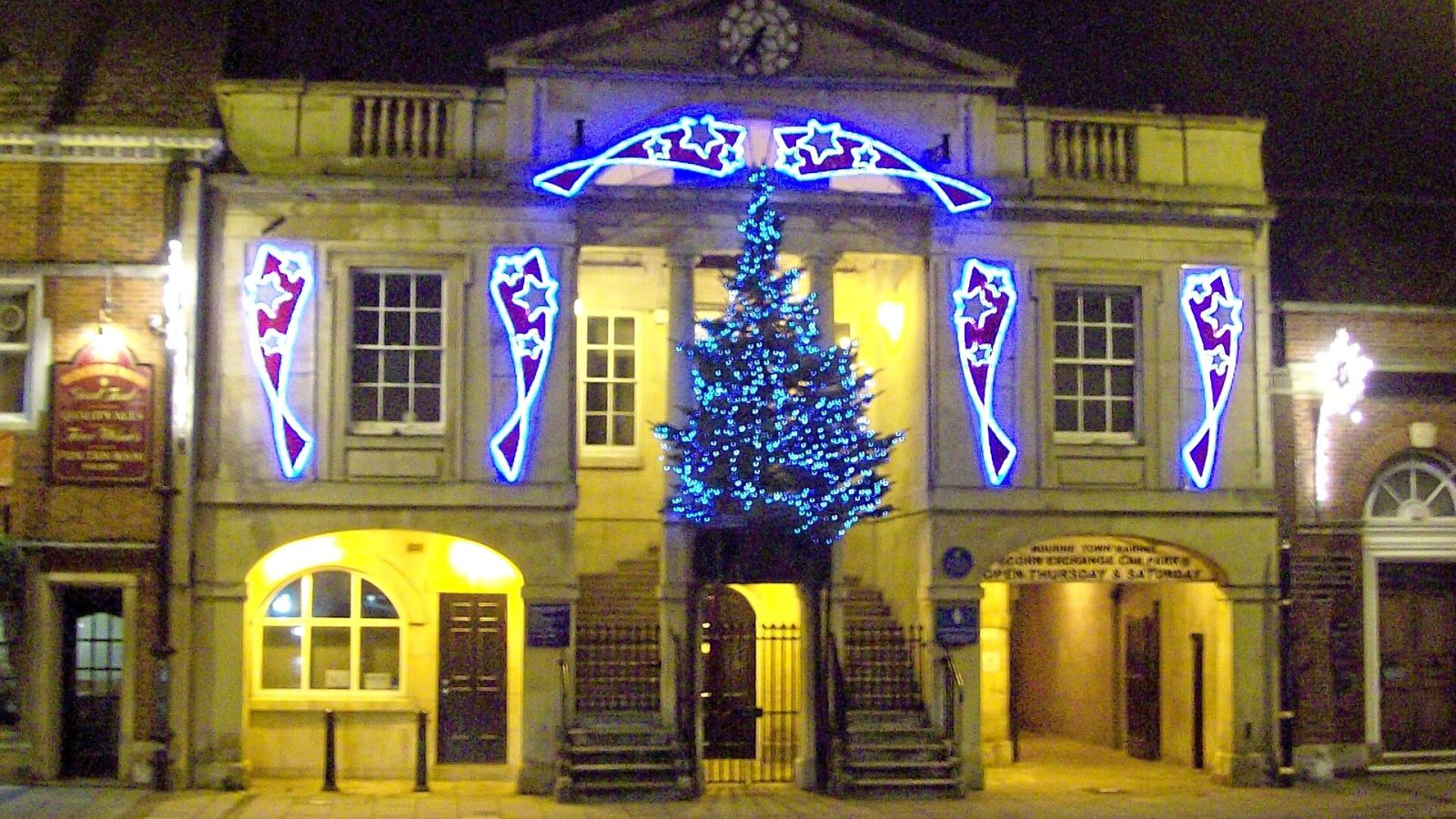 Fachada de prédio histórico decorada com luzes de Natal e árvore iluminada, à noite