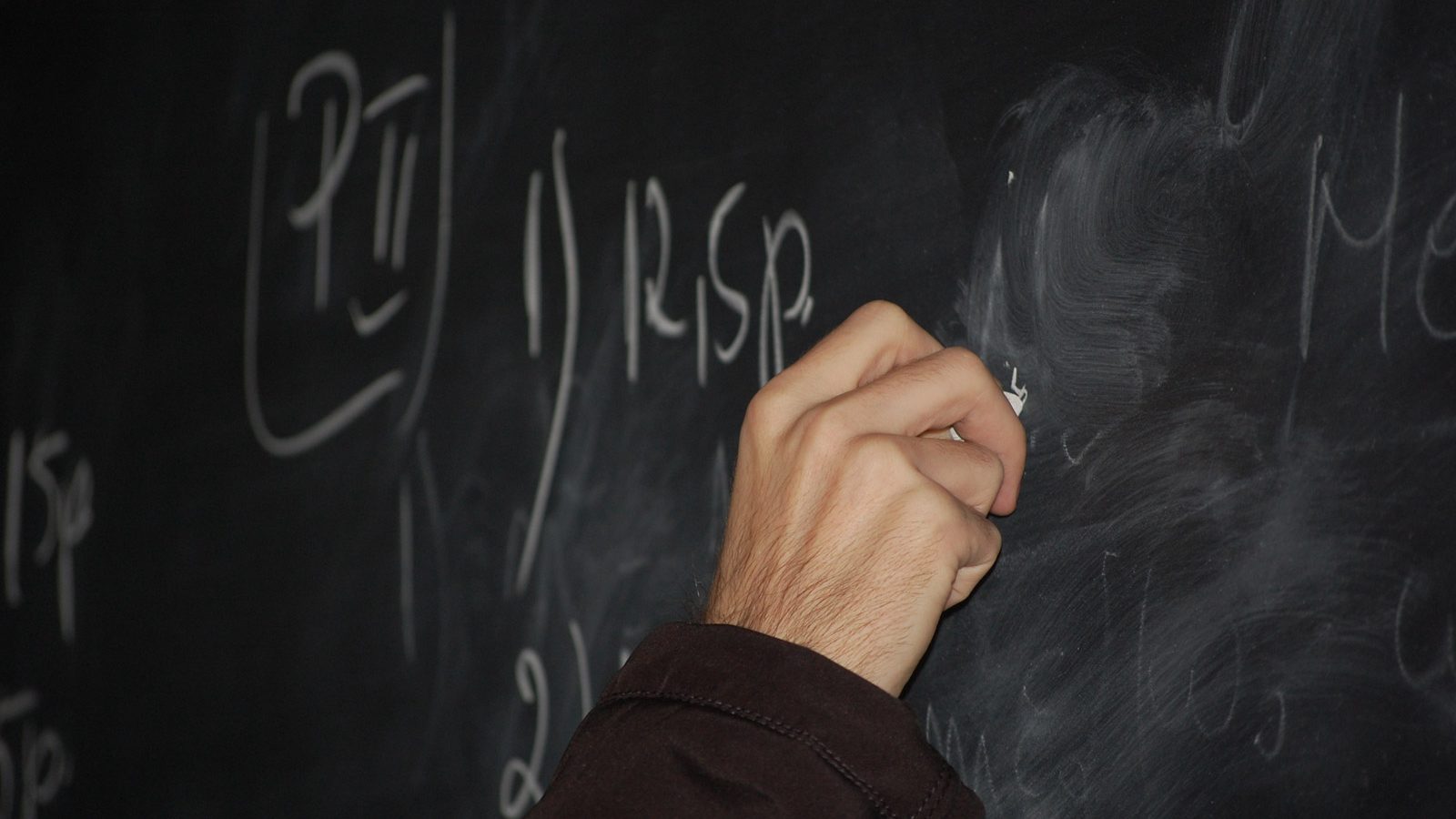 Mão escrevendo com giz em quadro-negro de sala de aula