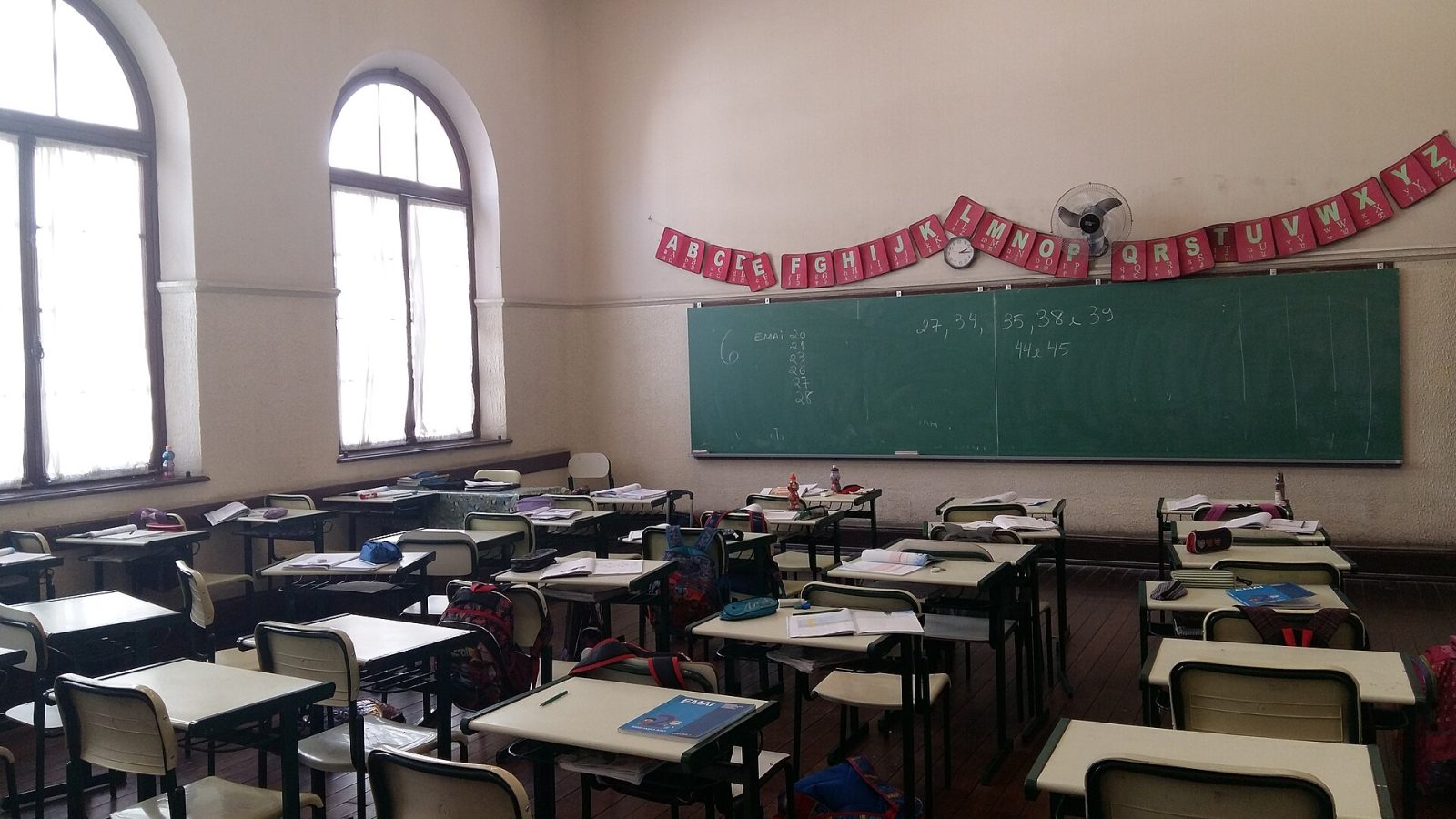 Sala de aula vazia de escola estadual, com fileiras de carteiras e quadro-verde ao fundo