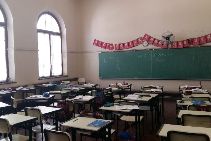Sala de aula vazia de escola estadual, com fileiras de carteiras e quadro-verde ao fundo