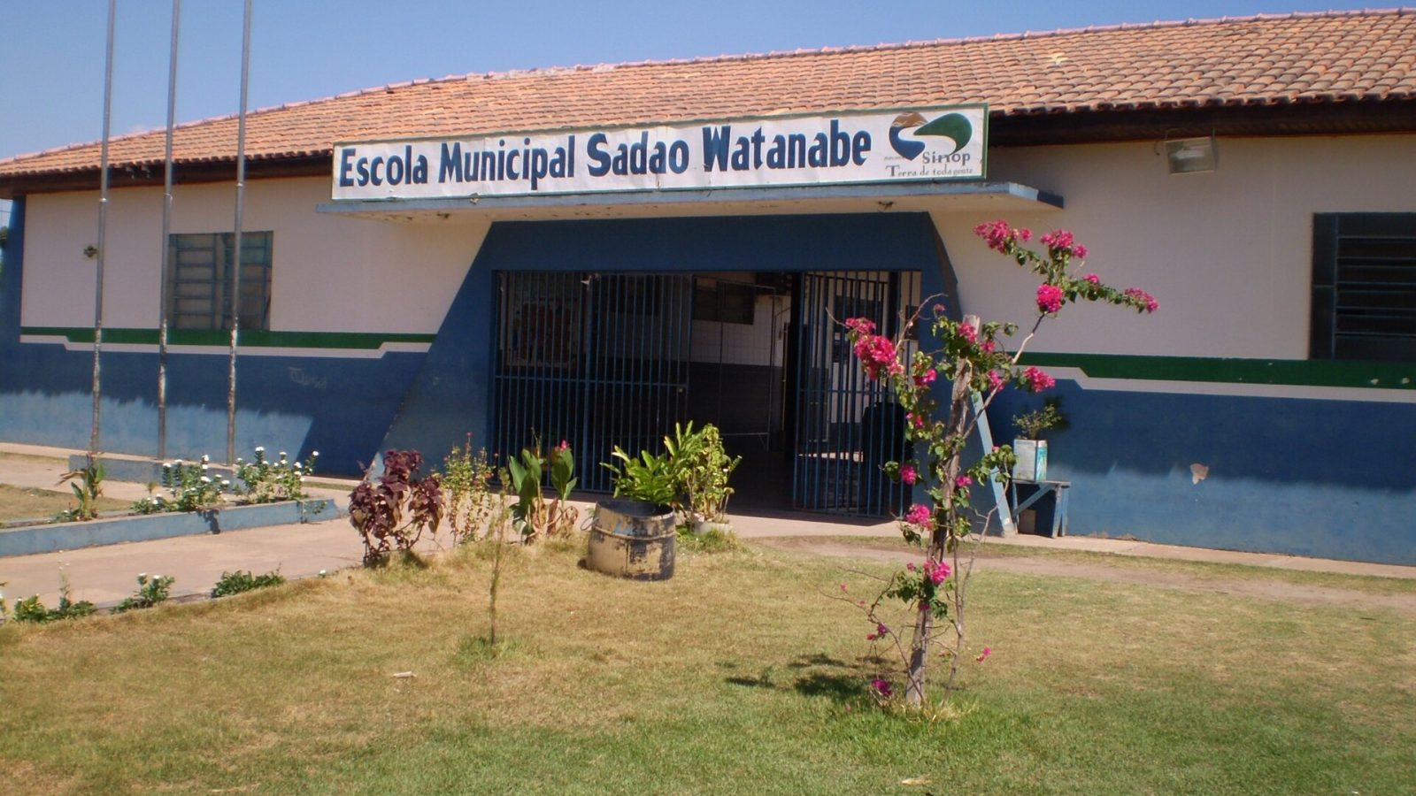 Fachada da Escola Municipal Sadao Watanabe, em Sinop, com gramado e uma buganvília florida diante da entrada