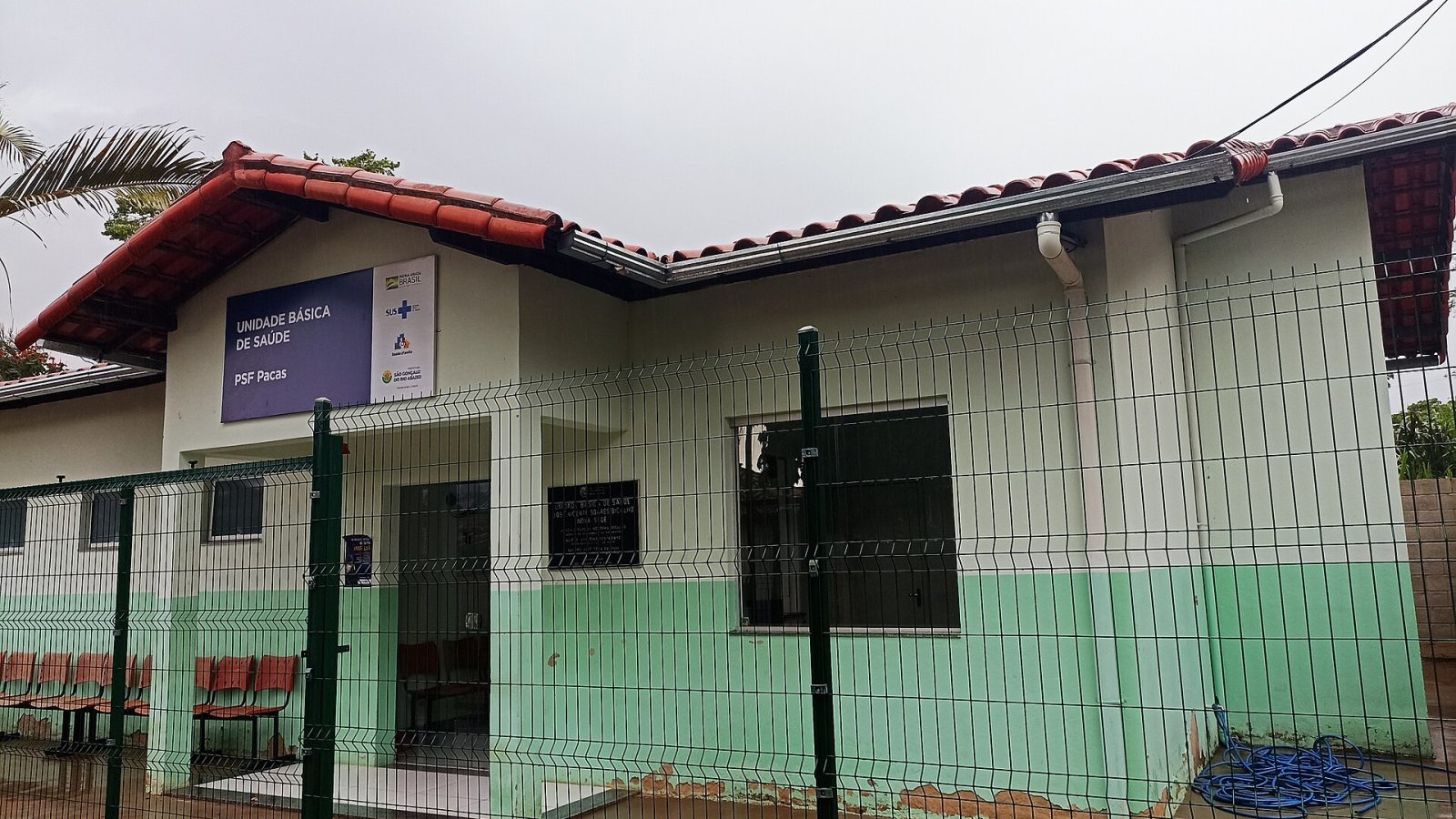 Fachada de uma Unidade Básica de Saúde térrea com telhado de cerâmica e grade verde