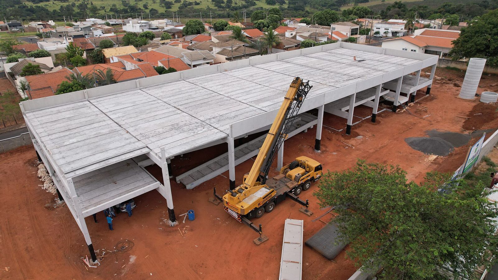 Vista aérea de canteiro de obras de um prédio escolar, com estrutura de concreto e guindaste
